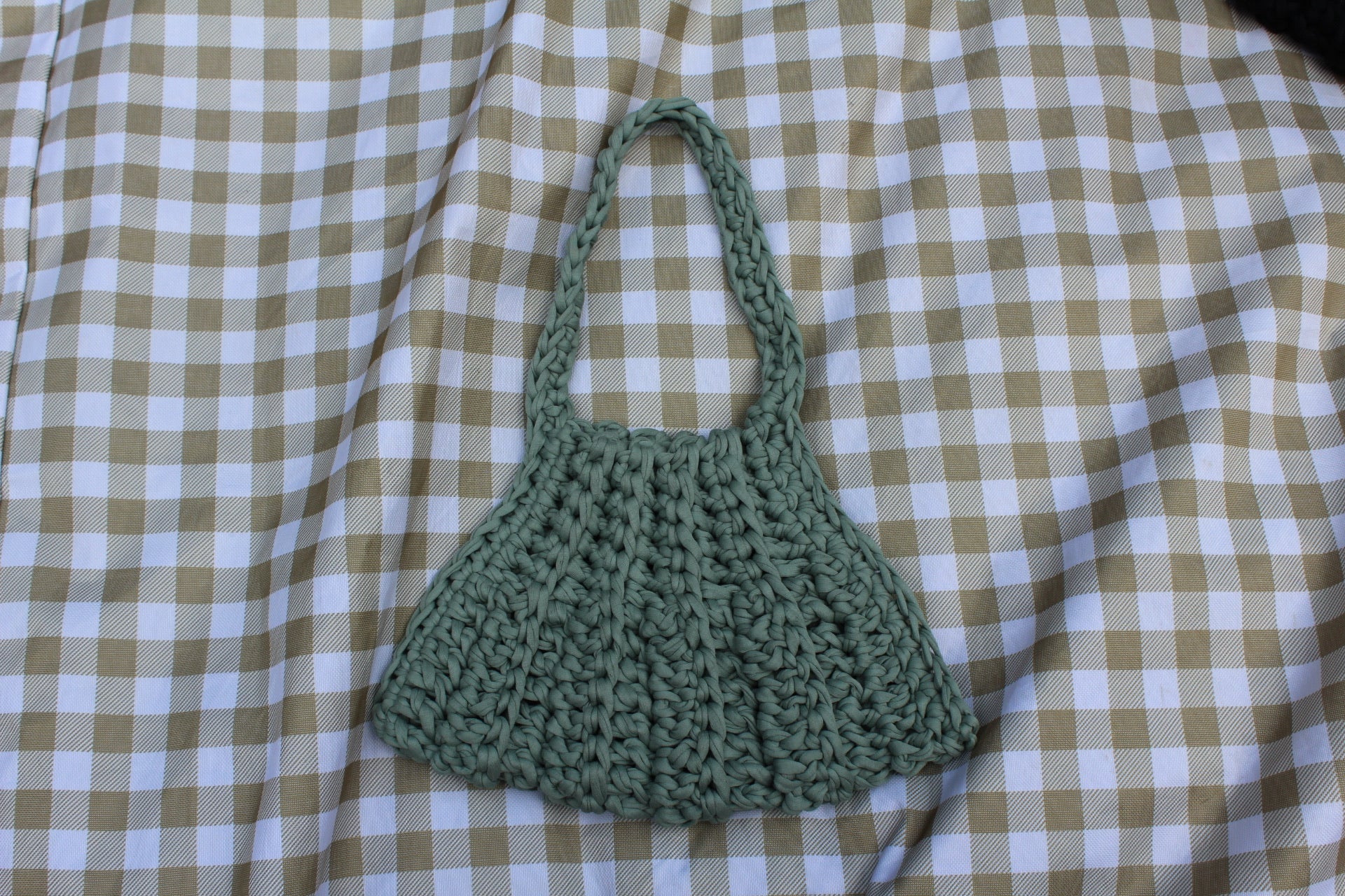 Green crocheted bag on a checkered fabric background